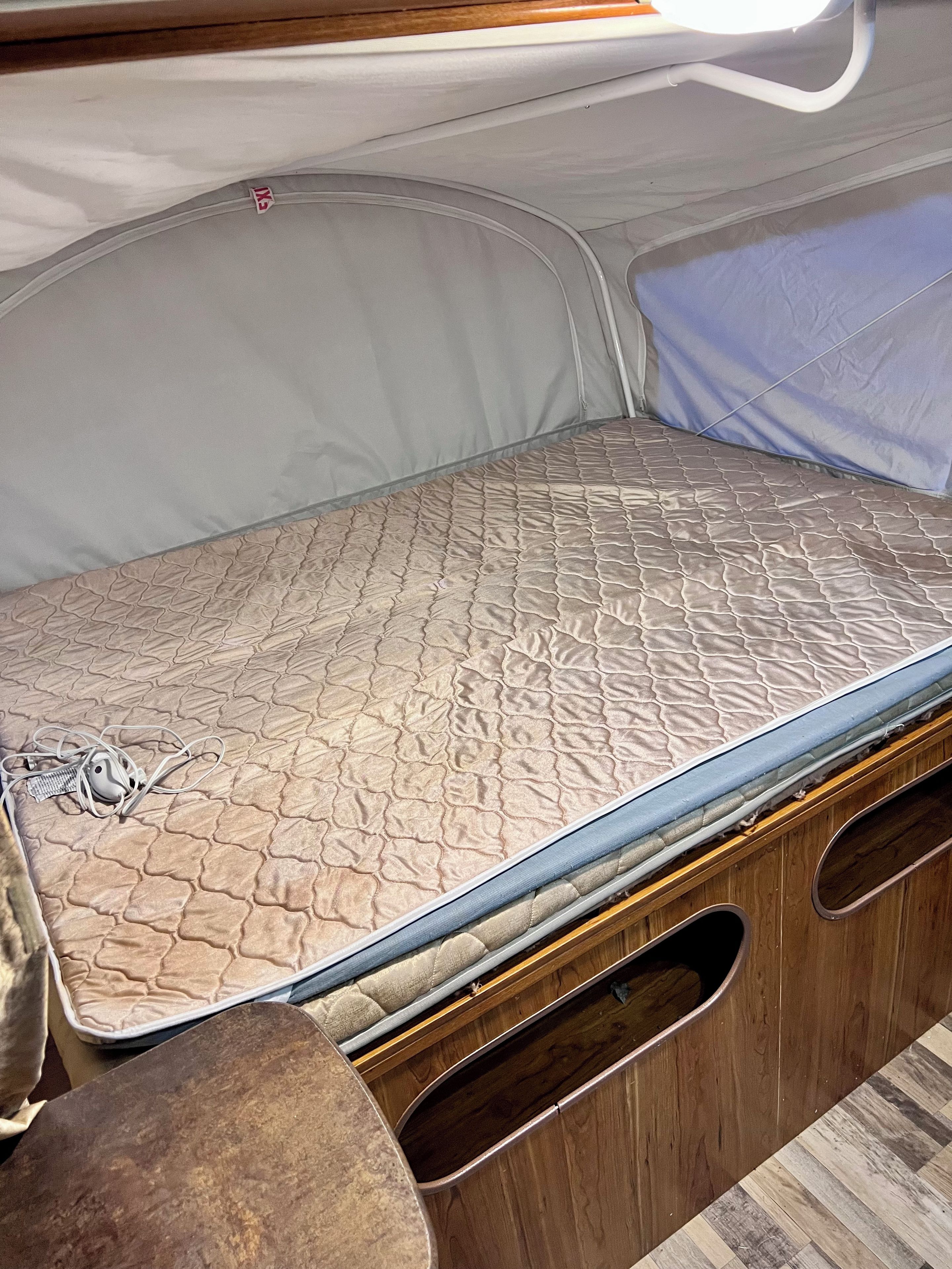 Ein platzsparendes Bett mit gesteppter Matratze und einem Kopfteil mit Reißverschluss.