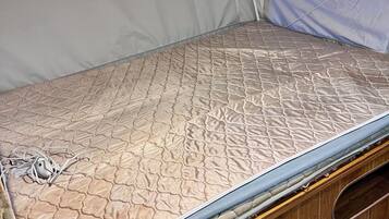 Ein platzsparendes Bett mit gesteppter Matratze und einem Kopfteil mit Reißverschluss.