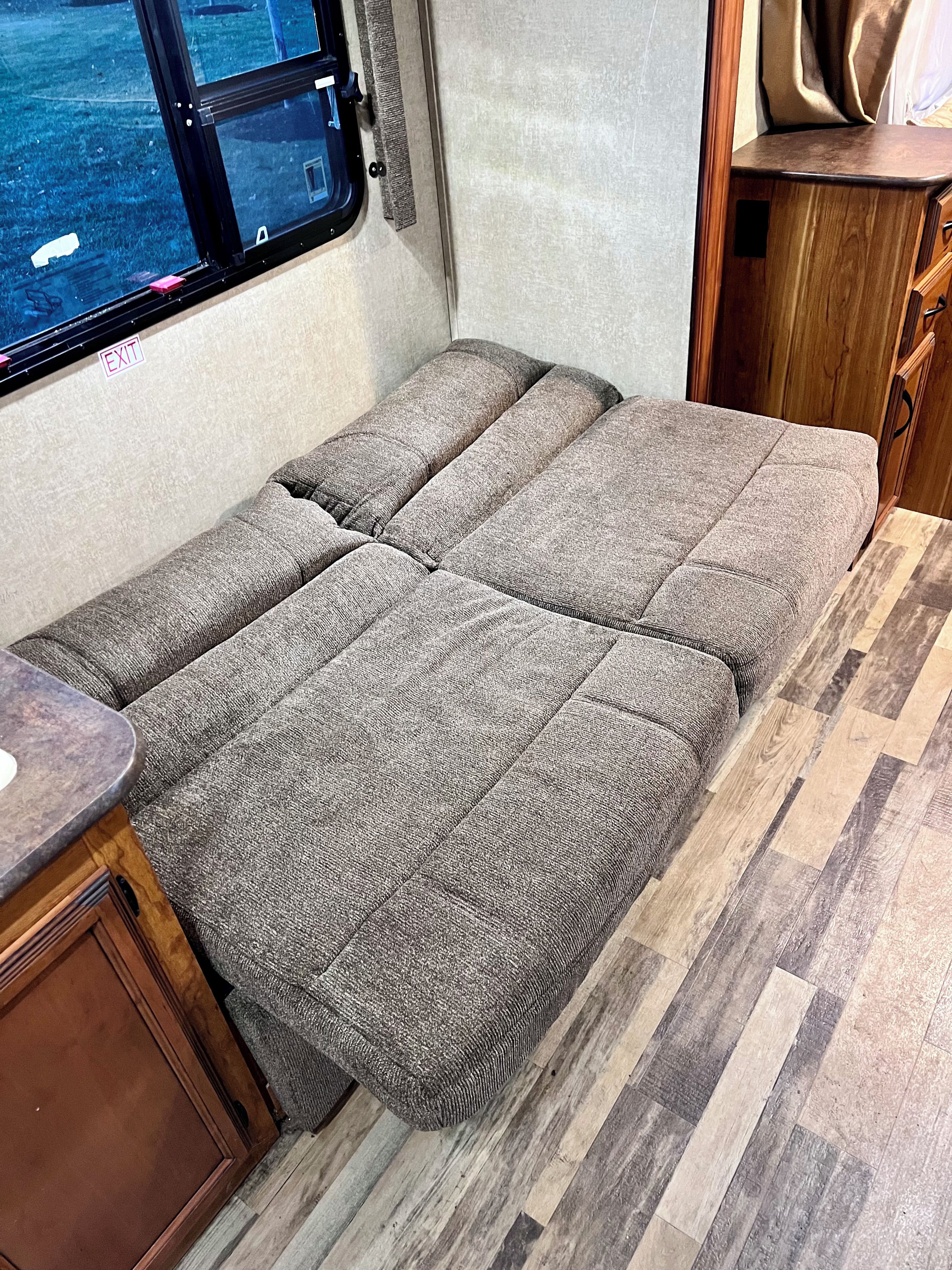 A compact RV interior with a foldable bed, a small kitchenette, and a window providing a view of the outdoors.