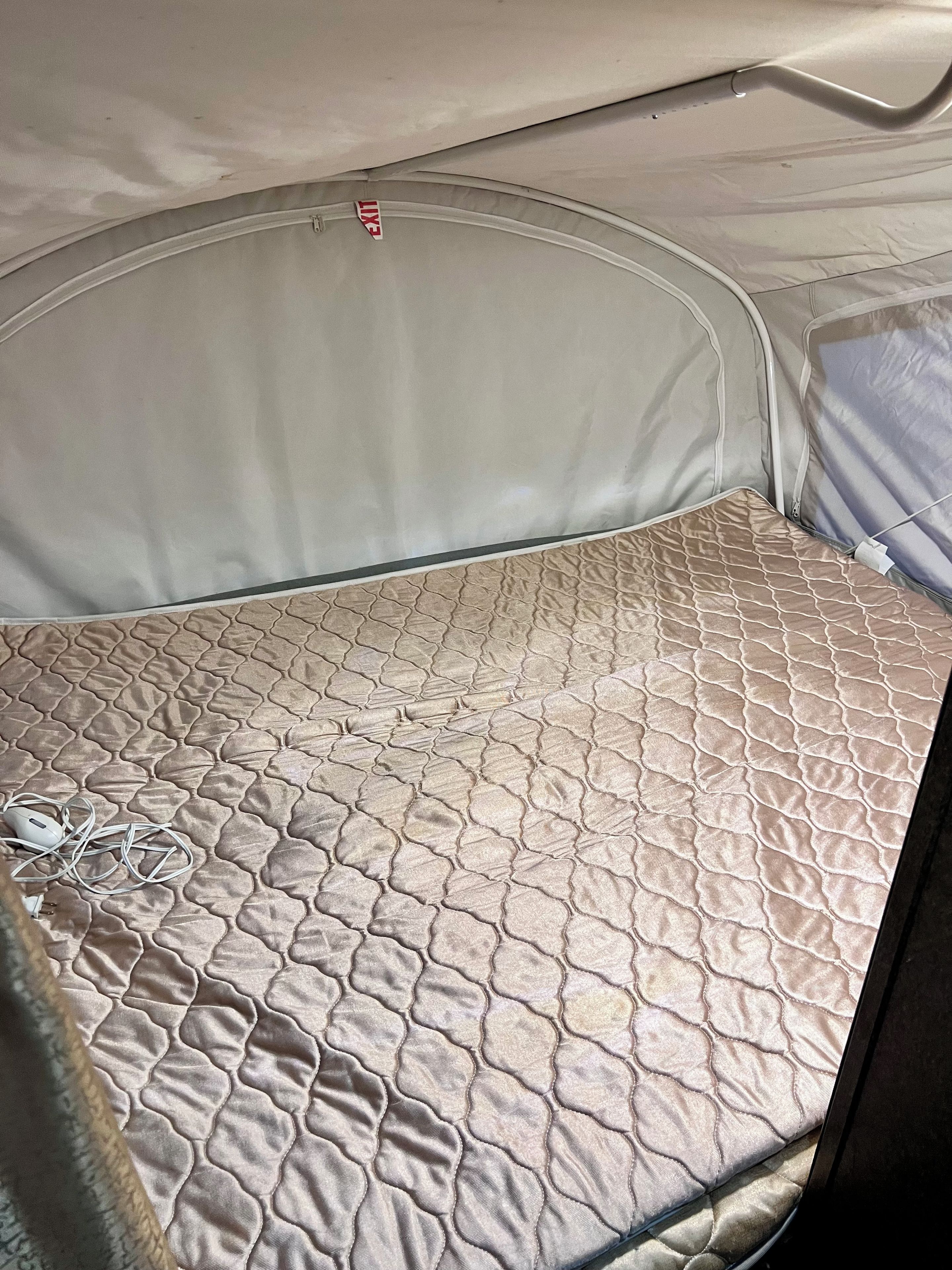 A tent with a quilted mattress and a visible exit sign.