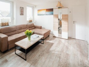 Una sala moderna con un sofá marrón, una mesa de centro de madera y un jarrón con flores amarillas.