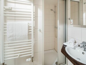 A bathroom with a white towel rack, a shower with a handheld showerhead, and a sink with a mirror. - Holiday Apartment With 1 Bedroom (Norderney)