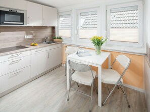 A modern kitchen with white cabinets, a built-in microwave, and a window with blinds. - Holiday Apartment With 1 Bedroom (Norderney)