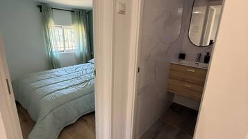 Un dormitorio con cama, un baño con espejo y una puerta que da a otra habitación.