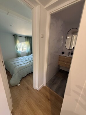 A bedroom with a bed, a bathroom with a mirror, and a door leading to another room.
