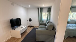 Ett modernt vardagsrum med en platt-TV, en bordsfläkt, en soffa och ett fönster med gardiner.