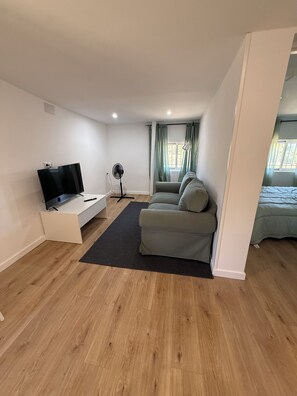 Een moderne woonkamer met een flatscreen televisie, een ventilator, een bank en een raam met gordijnen.
