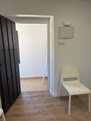 A room with a wooden floor, a white chair, a white wall, and a door with a metal handle.