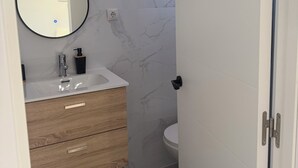 Ett badrum med ett vitt handfat, ett träfärgat tvättställ, väggar klädda med marmor och en spegel.