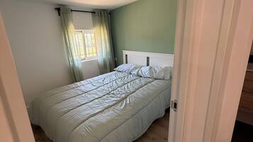 Een slaapkamer met een bed, een raam met gordijnen en een deur naar een andere kamer.