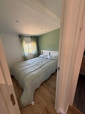 Une chambre à coucher avec un lit, une fenêtre avec des rideaux et une porte donnant sur une autre pièce.