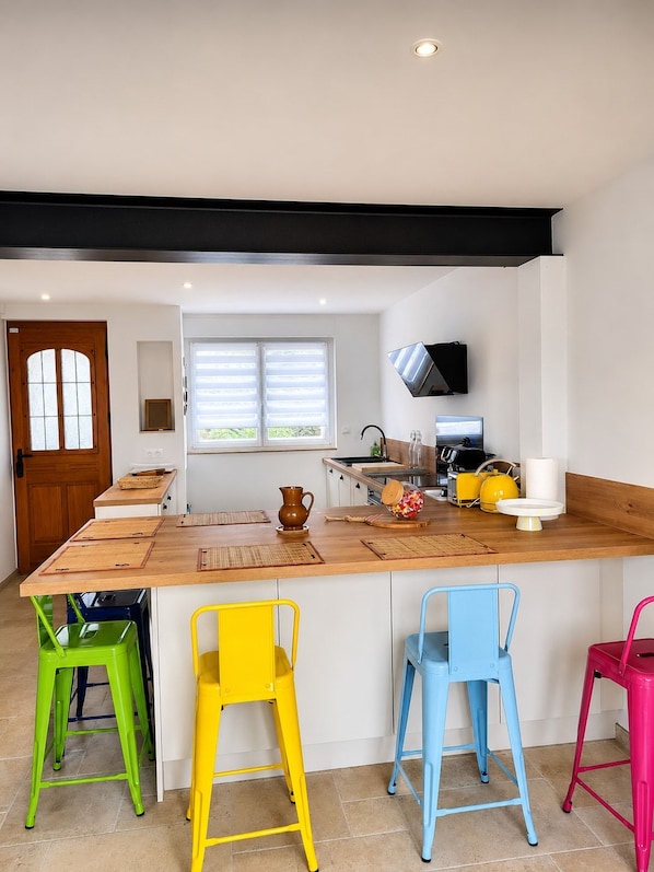 A modern kitchen with a wooden island, colorful bar stools, and a flat-screen TV mounted above the island.