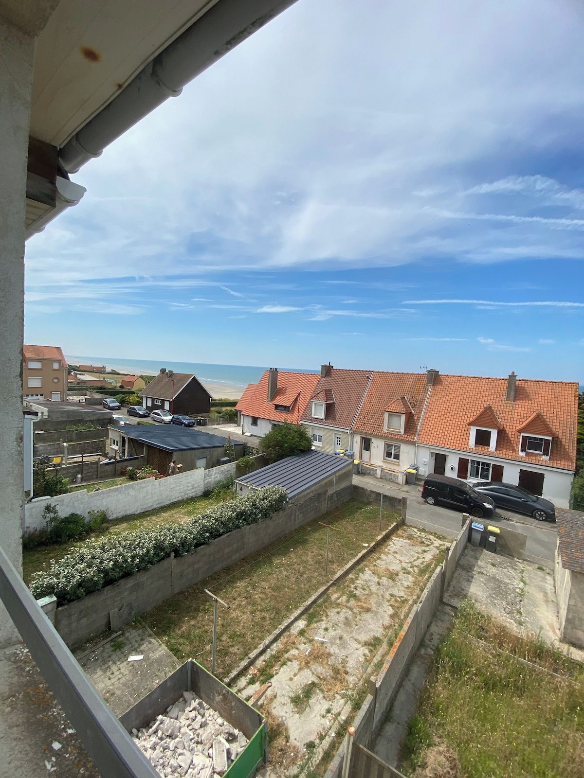 Un quartier résidentiel avec des maisons, un ciel dégagé et une plage qui se devine au loin.