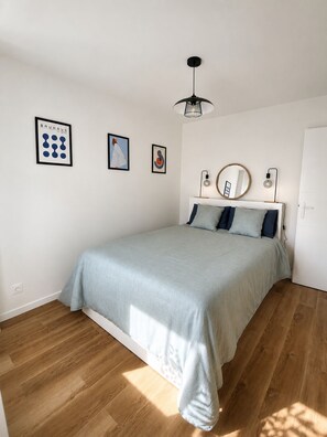 A bedroom with a bed, a wall-mounted light fixture, and framed artwork.