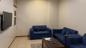 Una sala de estar con dos sofás azules, una mesa de centro, un televisor de pantalla plana y una lámpara de techo.