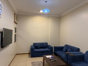 Ein Wohnzimmer mit zwei blauen Sofas, einem Couchtisch, einem Flachbildfernseher und einer Deckenleuchte.
