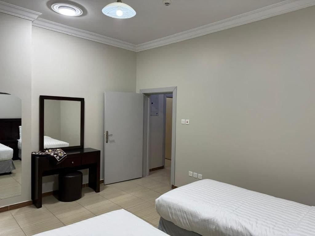 A hotel room with a bed, a bedside table with a mirror, a wardrobe, and a door leading to another room.