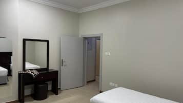 A hotel room with a bed, a bedside table with a mirror, a wardrobe, and a door leading to another room.