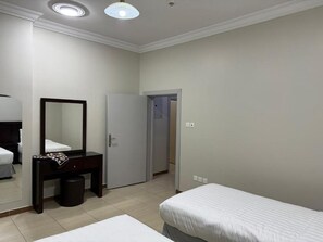 A hotel room with a bed, a bedside table with a mirror, a wardrobe, and a door leading to another room.