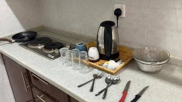 A kitchen counter with a kettle, a frying pan, a cutting board, and various utensils.