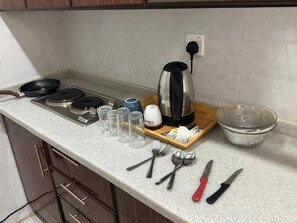 Una encimera de cocina con una tetera, una sartén, una tabla de cortar y varios utensilios.