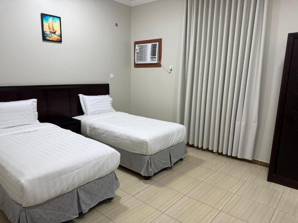A hotel room with two beds, a painting on the wall, an air conditioning unit, and a window with curtains.