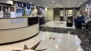 Un vestíbulo de hotel con una recepción, un área de estar y una escalera que conduce al piso superior.
