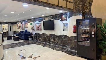 A lobby with a marble floor, seating area, vending machine, and a wall-mounted television.