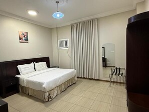 Habitación de hotel con cama, mesita de noche, espejo, ventana con cortinas y aire acondicionado.
