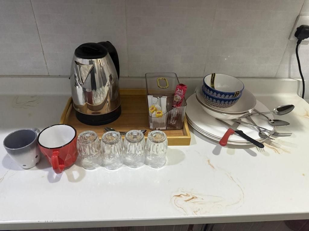 A kitchen counter with a kettle, a red mug, salt and pepper shakers, a box of tissues, a bowl, and cutlery.