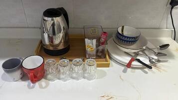 A kitchen counter with a kettle, a red mug, salt and pepper shakers, a box of tissues, a bowl, and cutlery.