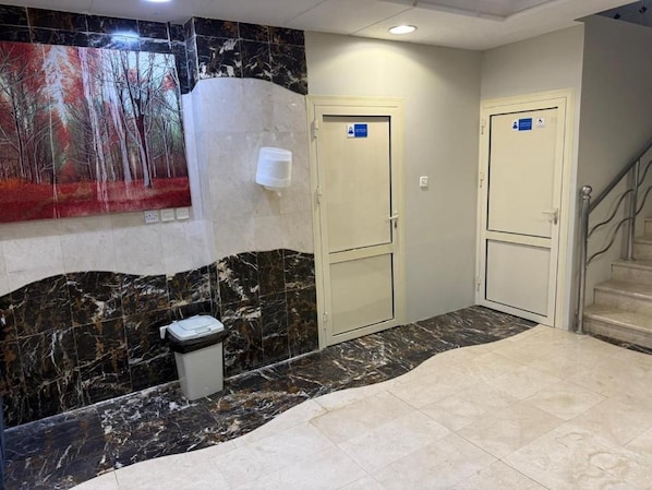 A hotel lobby with marble flooring, a trash bin, two doors with blue signs, and a staircase.
