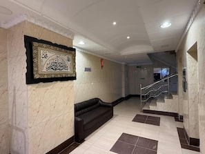A lobby with a marble wall, a black leather sofa, and a staircase.