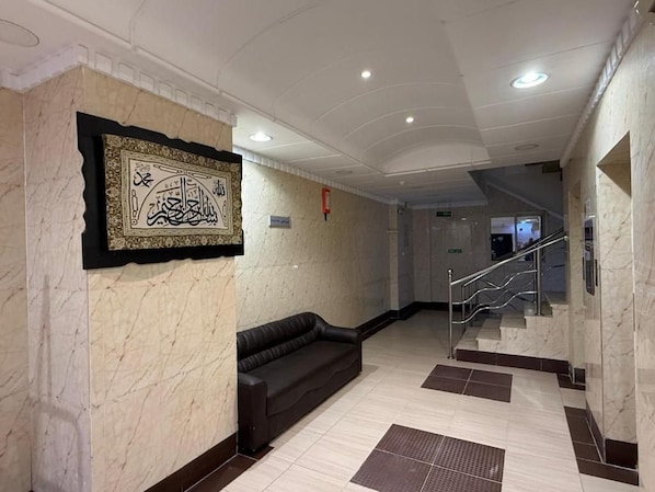 A lobby with a marble wall, a black leather sofa, and a staircase.