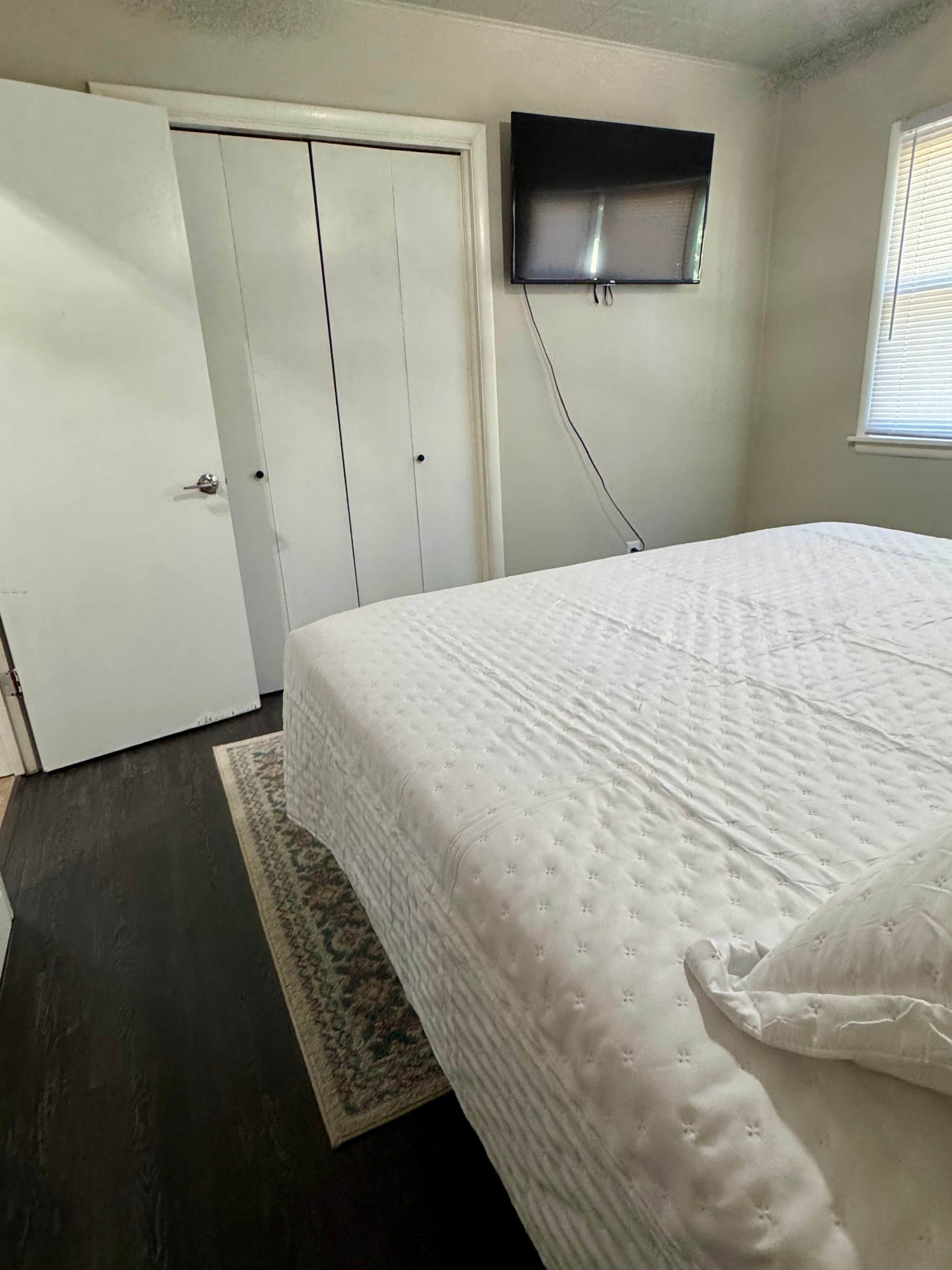 Una camera da letto con un letto, un armadio, una televisione a parete e una finestra con persiane.