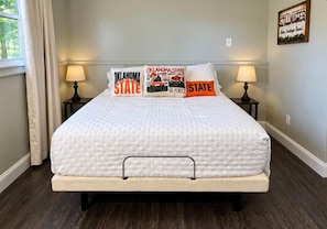 Una cama con una colcha blanca acolchada, dos lámparas de noche y tres almohadas con el texto 'Oklahoma State'.