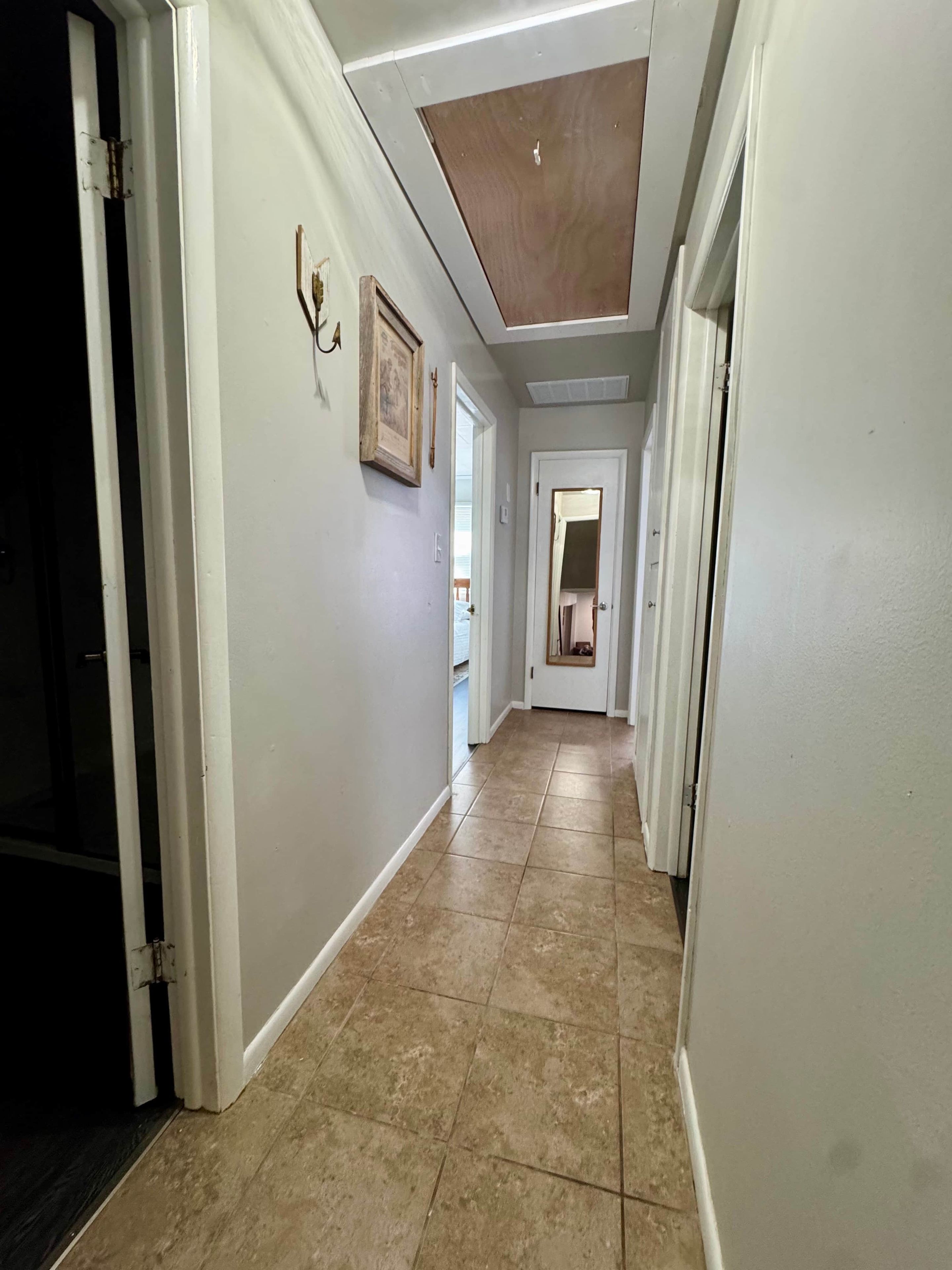 A hallway with white walls, a wooden ceiling, and a tiled floor.