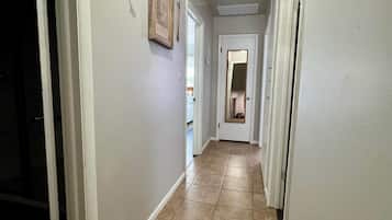 A hallway with white walls, a wooden ceiling, and a tiled floor.