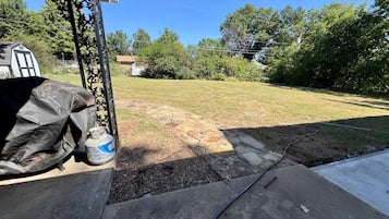 A backyard with a stone pathway leading to a house, a covered grill, and a hose on the ground.