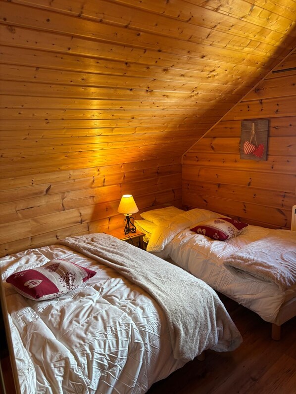 Une chambre confortable située sous les toits, avec deux lits, une lampe et des murs en bois.
