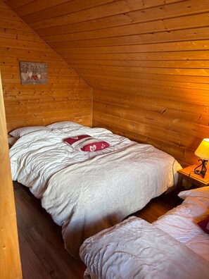 A single bed with a white comforter and a red heart-shaped pillow in a wooden cabin room.