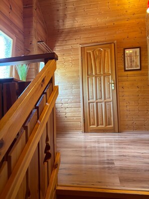 Un interior de madera con una escalera, una puerta de madera y un cuadro enmarcado en la pared.