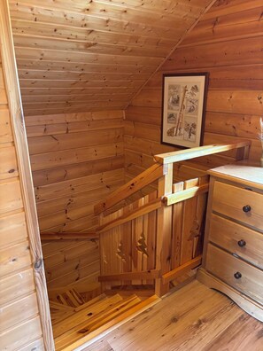 A wooden interior with a staircase, a dresser, and a framed picture on the wall.