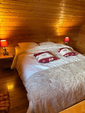 A cozy room with wooden walls and a bed with white bedding and decorative pillows. There are two bedside tables with lamps.