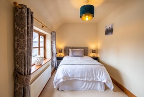 A bedroom with a bed, bedside lamps, a window with curtains, a radiator, and a wall-mounted picture.