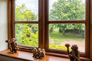 A window with a view of a garden and three monkey figurines on the sill.