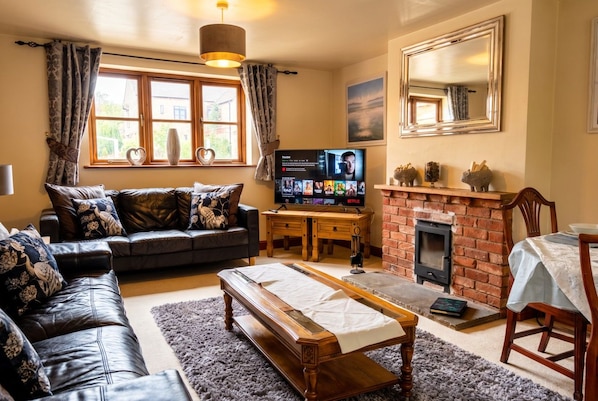 A cozy living room with a leather sofa, a wooden coffee table, a fireplace, and a television.