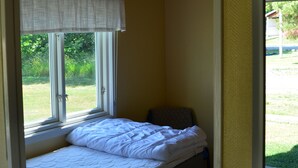 A single bed with a white duvet and a window with a white curtain. - Grönhögens Stugby (Degerhamn)