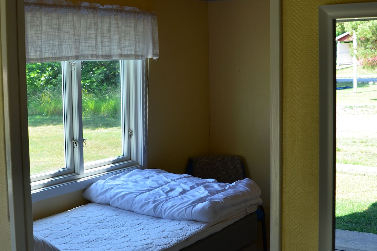 A single bed with a white duvet and a window with a white curtain.