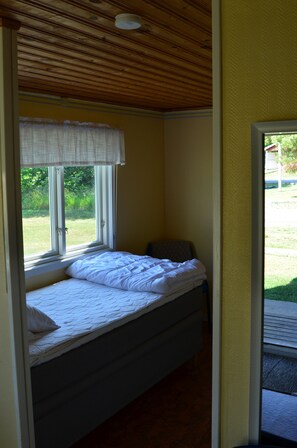 A single bed with a white duvet and a window with a white curtain. - Grönhögens Stugby (Degerhamn)